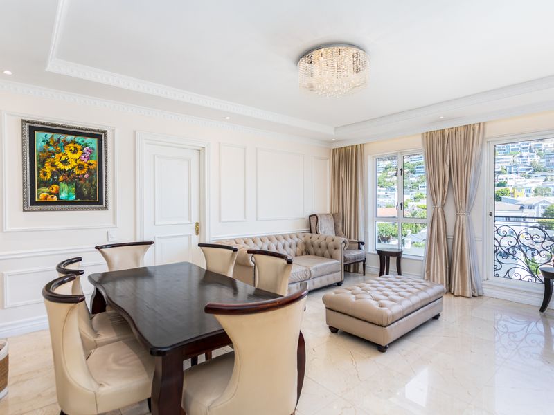 Elegant open-plan living and dining area featuring sophisticated wainscoting, crown molding, polished marble floors, and a crystal chandelier with access to a private balcony.