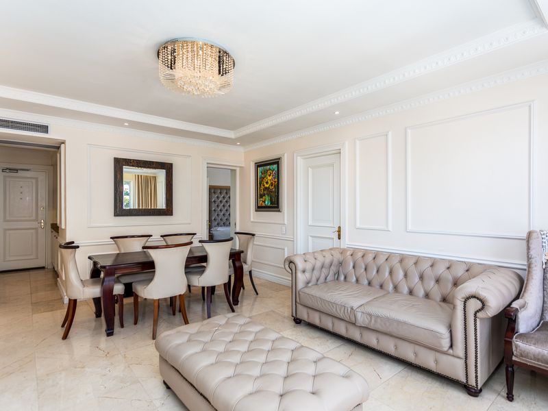 Elegant open-plan living and dining area featuring polished marble flooring, intricate crown molding, wainscoting, and a sophisticated crystal chandelier.