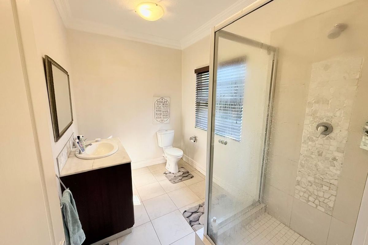 A functional bathroom featuring a glass-enclosed shower with mosaic tile accents, a vanity with a basin, and a standard toilet.