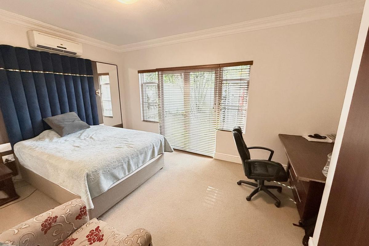 Spacious bedroom featuring neutral carpeting, a wall-mounted air conditioning unit, and large windows with fitted blinds providing natural light.