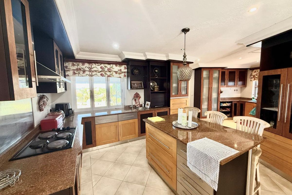 Spacious kitchen featuring a large central island with granite countertops, custom cabinetry, built-in cooktop, and tiled flooring.