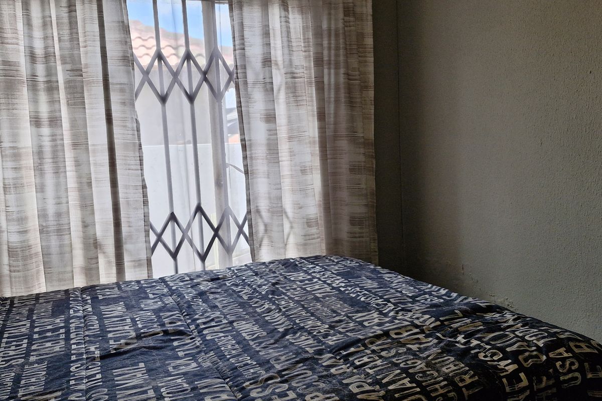 A bedroom featuring a window with a security gate and curtains, providing natural light and basic functional space.