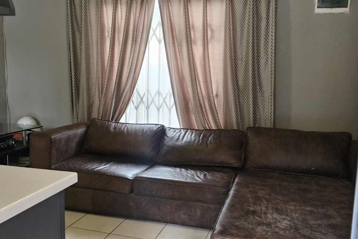 A living area featuring tiled flooring, a window with security gate, and a neutral wall finish.
