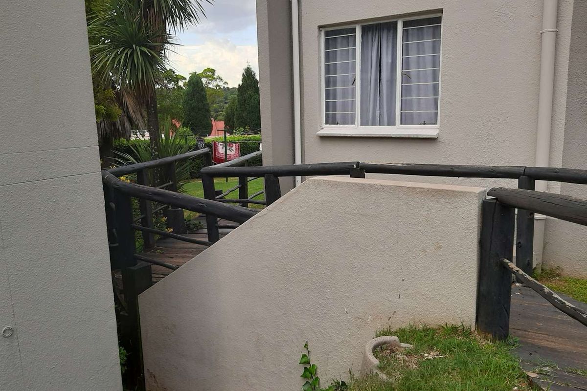 Rear exterior view of the apartment featuring a timber deck walkway with balustrades and a window with security bars.