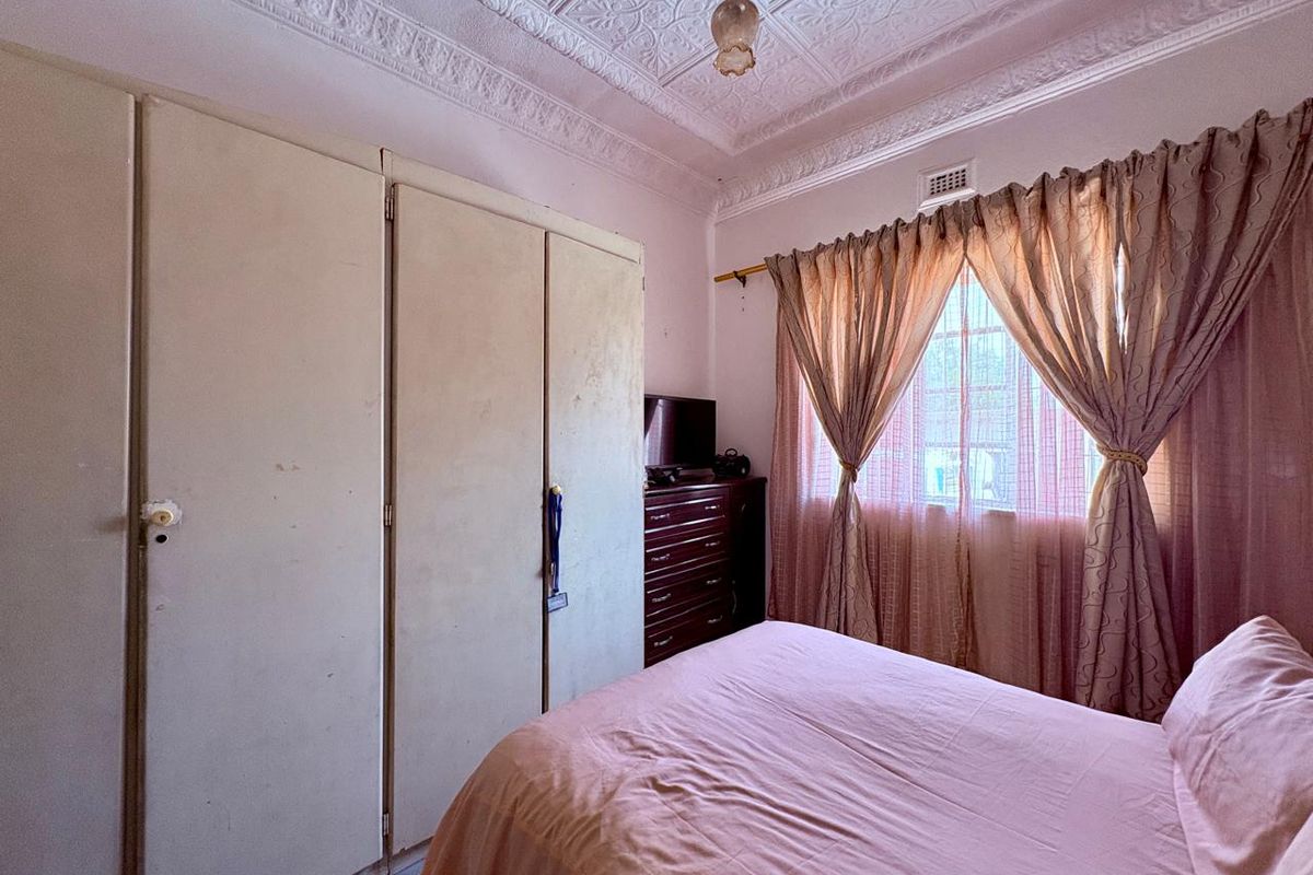 A bedroom featuring built-in wardrobes, decorative pressed metal ceiling, and a window with curtain treatments.
