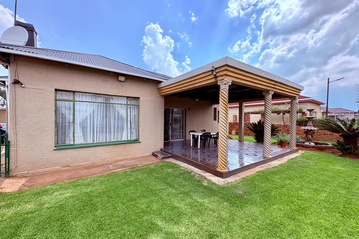 Rear view of the house featuring a covered patio with decorative columns, tiled flooring, and a well-maintained garden area.