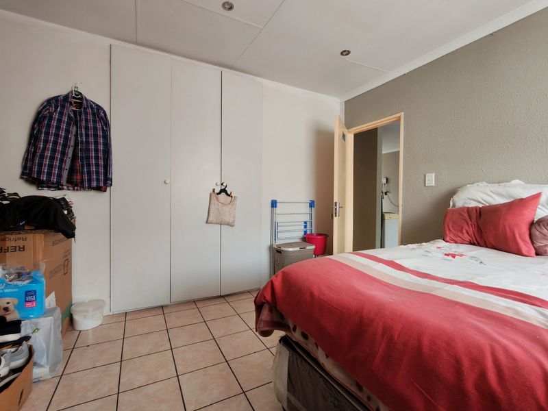 A bedroom featuring tiled flooring, built-in cupboards, and recessed ceiling lighting, offering a functional space with potential for cosmetic updates.