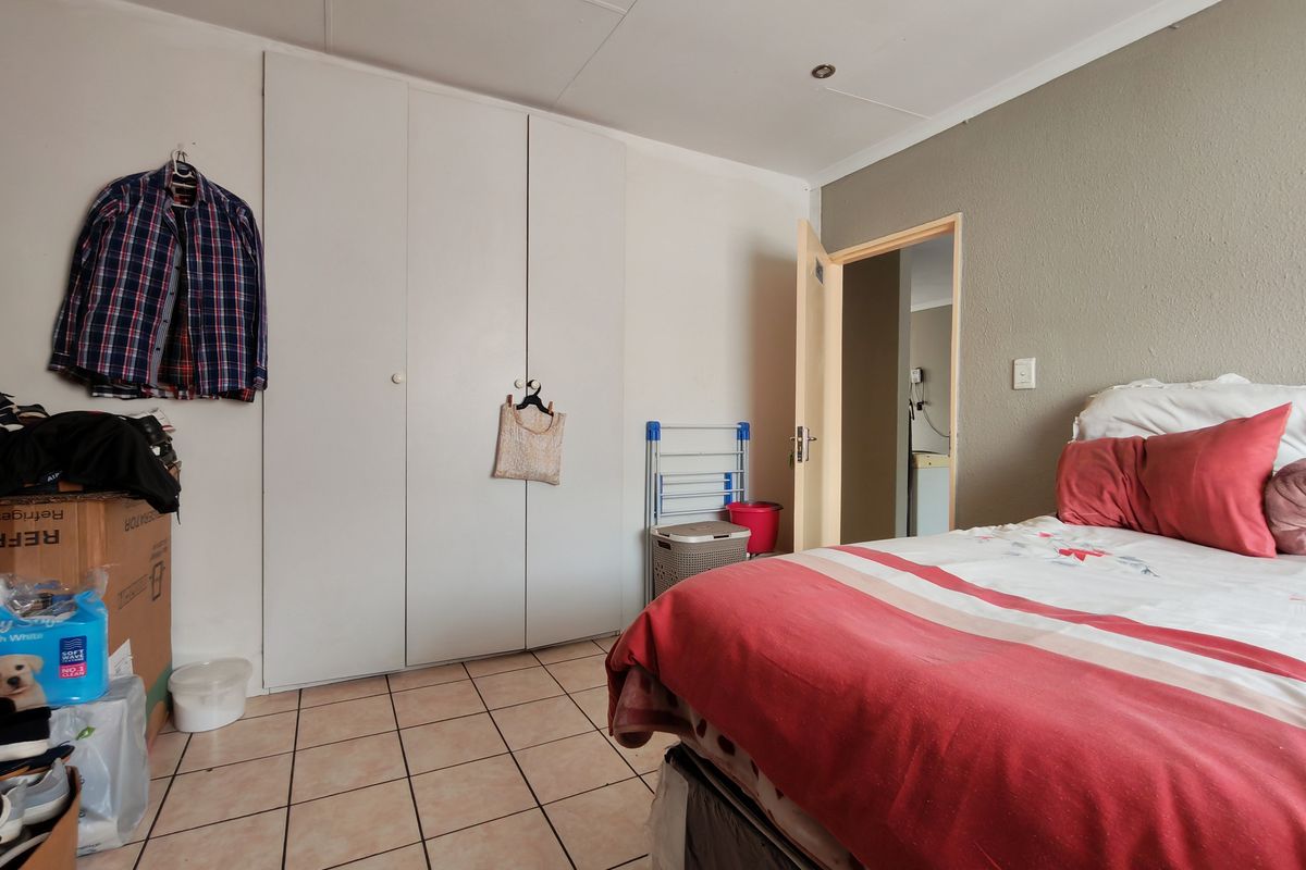 A bedroom featuring tiled flooring, built-in cupboards, and recessed ceiling lighting, offering a functional space with potential for cosmetic updates.