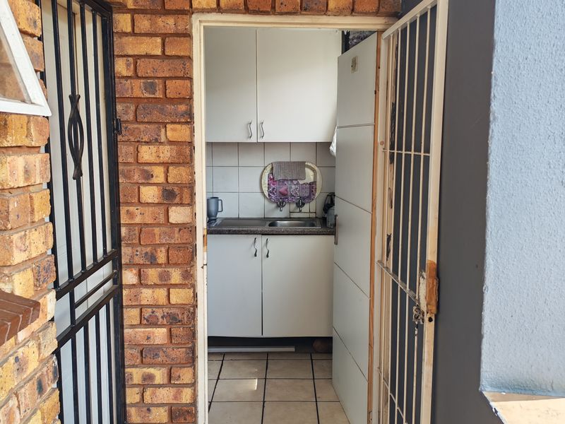 A functional scullery area featuring built-in cabinetry, a stainless steel sink, and tiled flooring, accessed through a secure metal gate.