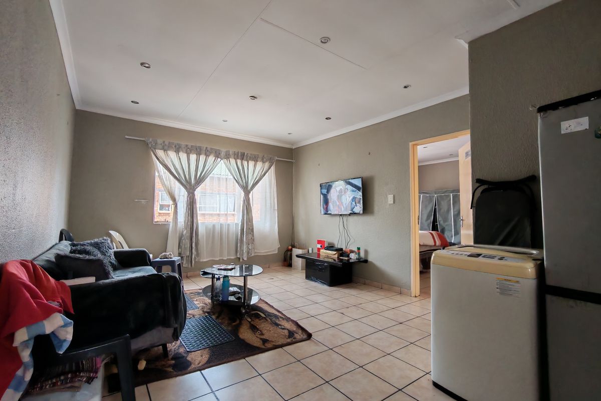 A living room featuring tiled flooring and recessed ceiling lighting, providing a functional space with direct access to an adjacent bedroom.
