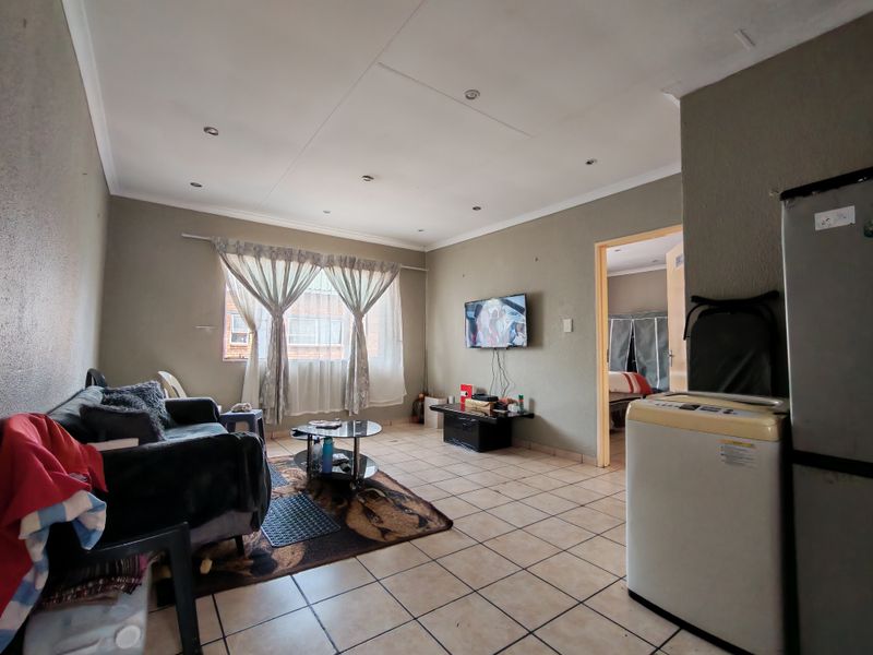 A living room featuring tiled flooring and recessed ceiling lighting, providing a functional space with direct access to an adjacent bedroom.
