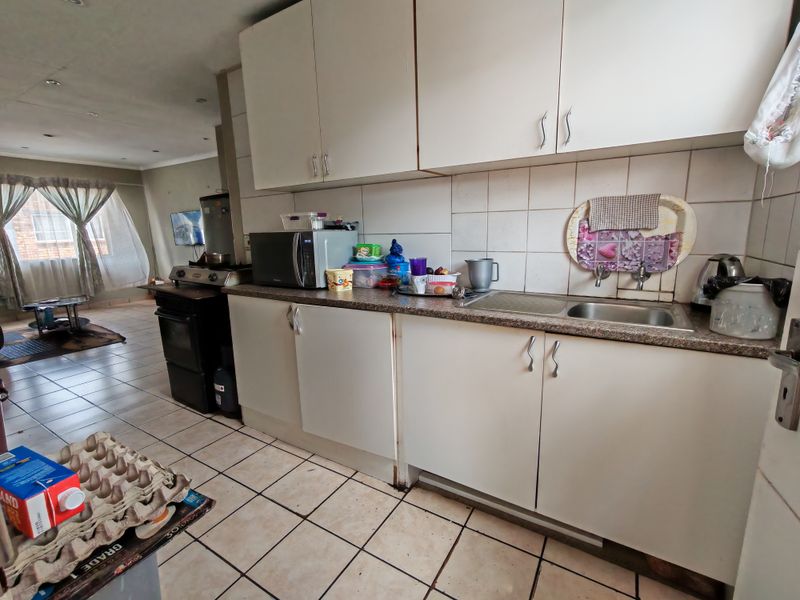 Open-plan kitchen area featuring built-in cabinetry, tiled backsplash, and tiled flooring, flowing into the adjacent living space.