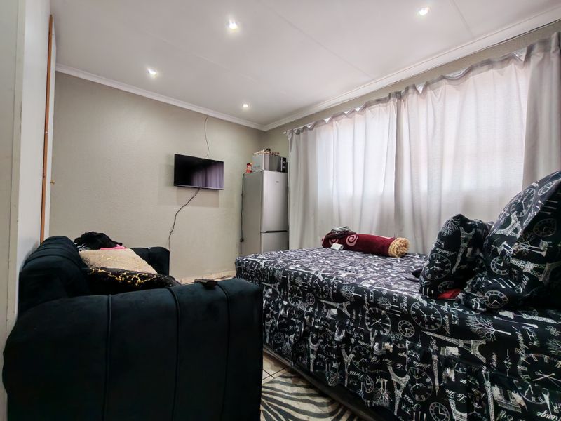 A compact bedroom featuring tiled flooring, recessed ceiling lighting, and window curtain tracks, providing a functional living space.