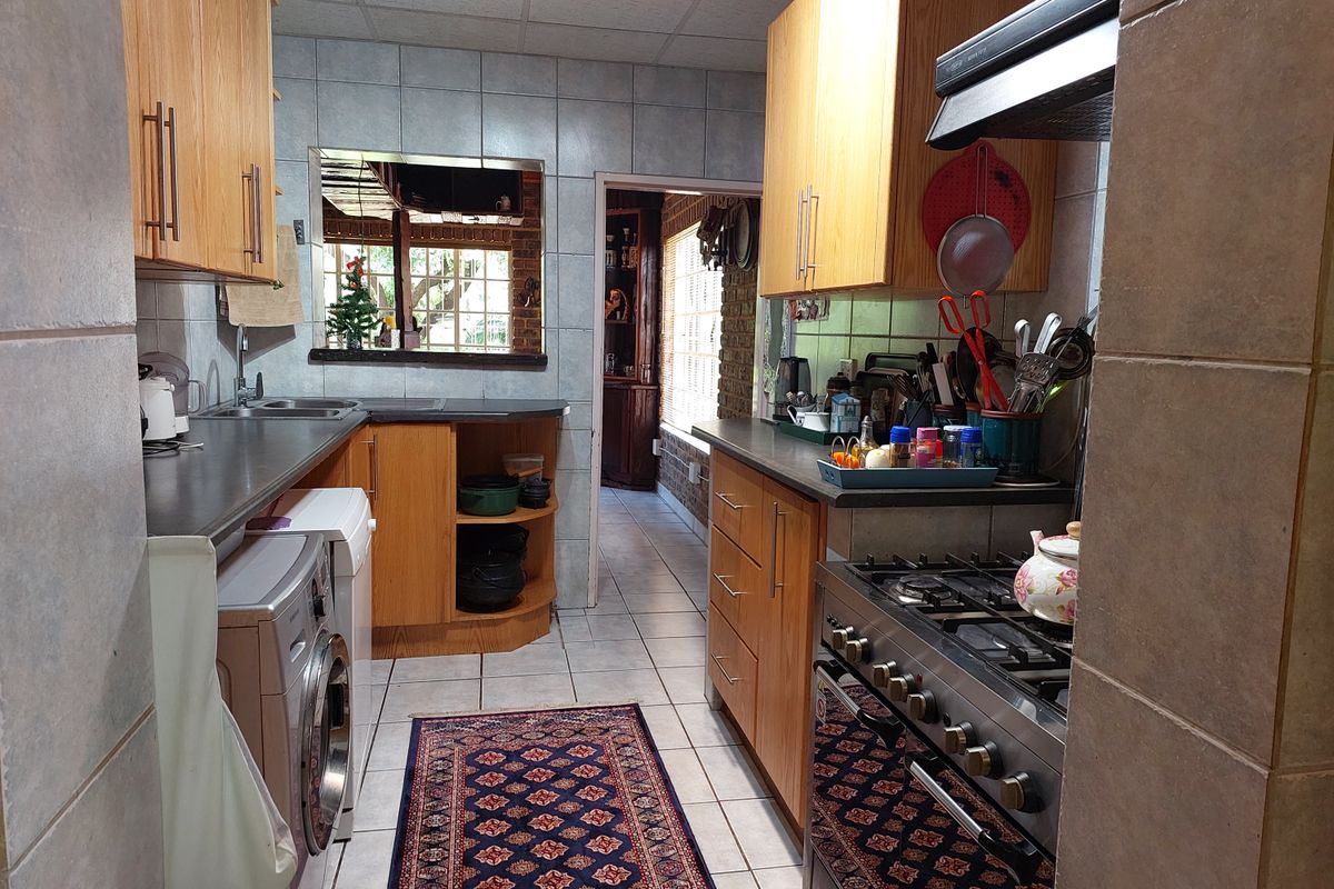 Functional kitchen featuring wooden cabinetry, gas stove with extractor fan, tiled flooring, and integrated laundry space with direct access to adjacent living areas.