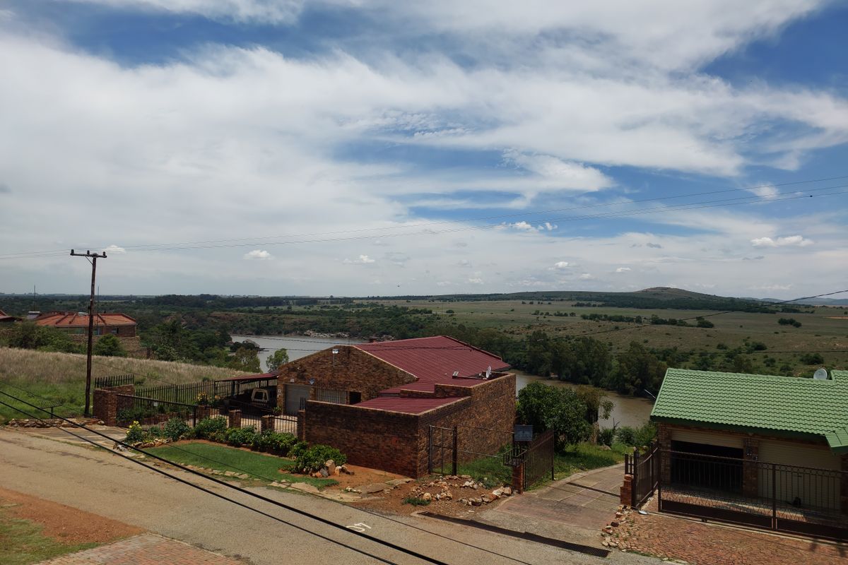 Elevated view of a residential property featuring face-brick construction, metal roofing, and a scenic outlook over the surrounding landscape and river.