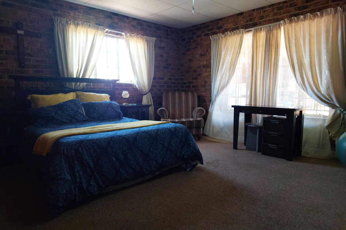 Spacious bedroom featuring exposed face-brick walls, large windows with natural light, and carpeted flooring.
