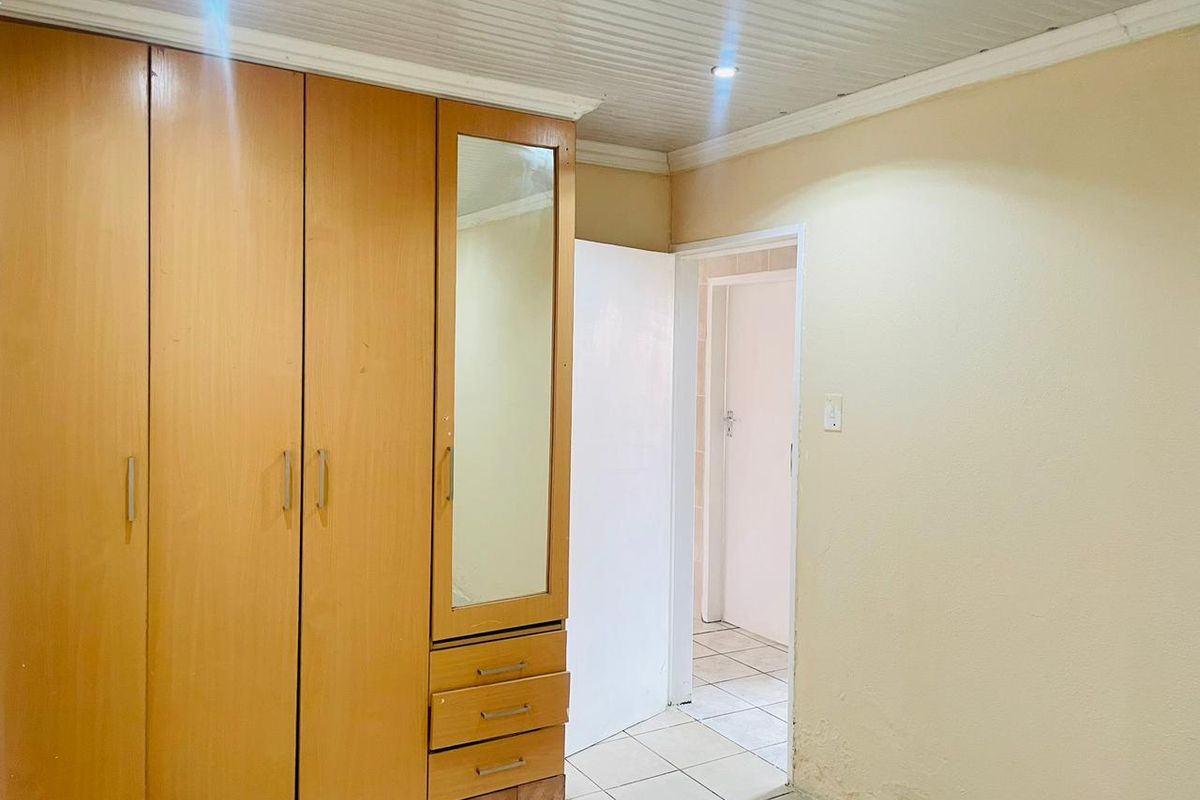 A bedroom featuring built-in wooden cabinetry with a mirrored section, tiled flooring, and a doorway leading to an adjacent room.