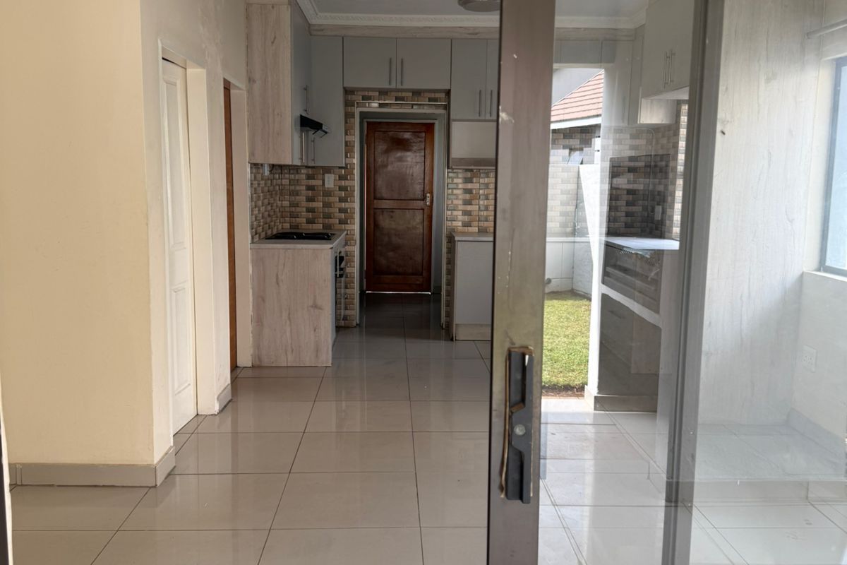 A view through a sliding glass door into a tiled kitchen area featuring built-in cabinetry, a hob, and an extractor fan.