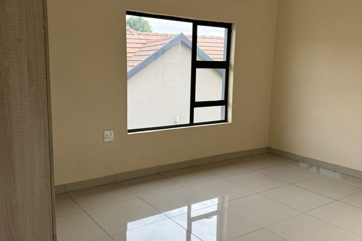 A bright, empty bedroom featuring neutral tiled flooring, built-in cabinetry, and a modern window with black frames.