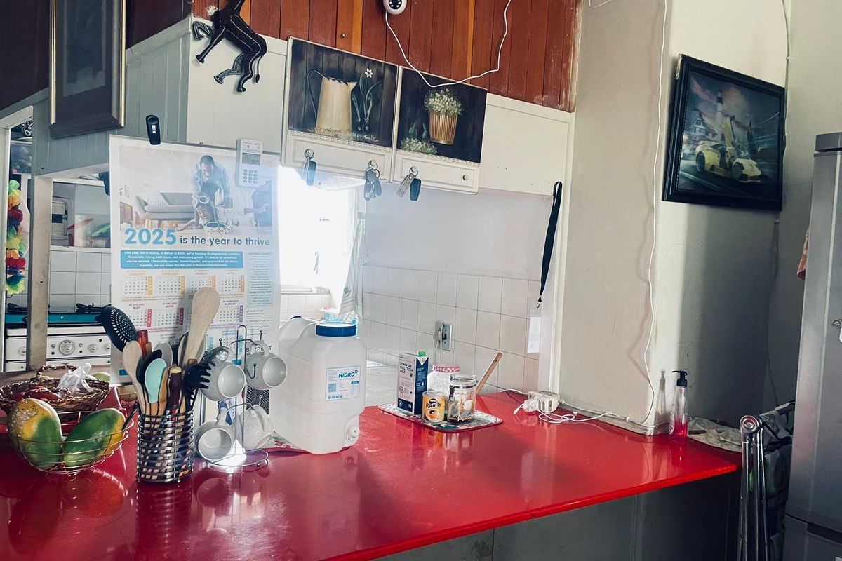A kitchen area featuring a red countertop, built-in cabinetry, and tiled splashback, showing signs of age and dated finishes.