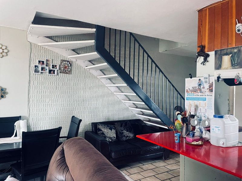 Open plan living area featuring a distinctive staircase with metal railings, tiled flooring, and a functional kitchen counter space.