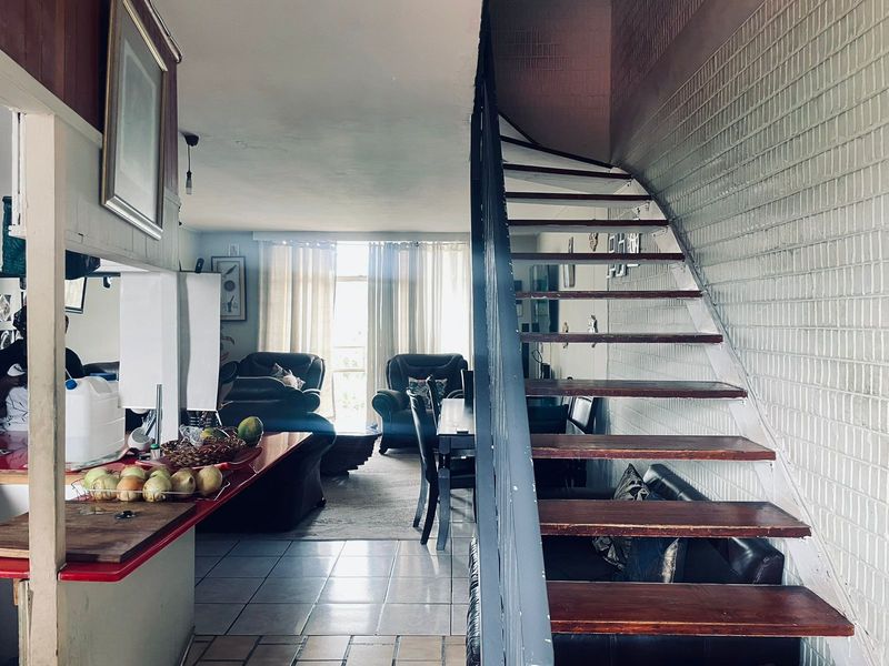 Open plan living area featuring a staircase with wooden treads, tiled flooring, and a kitchen counter, creating a functional and connected living space.