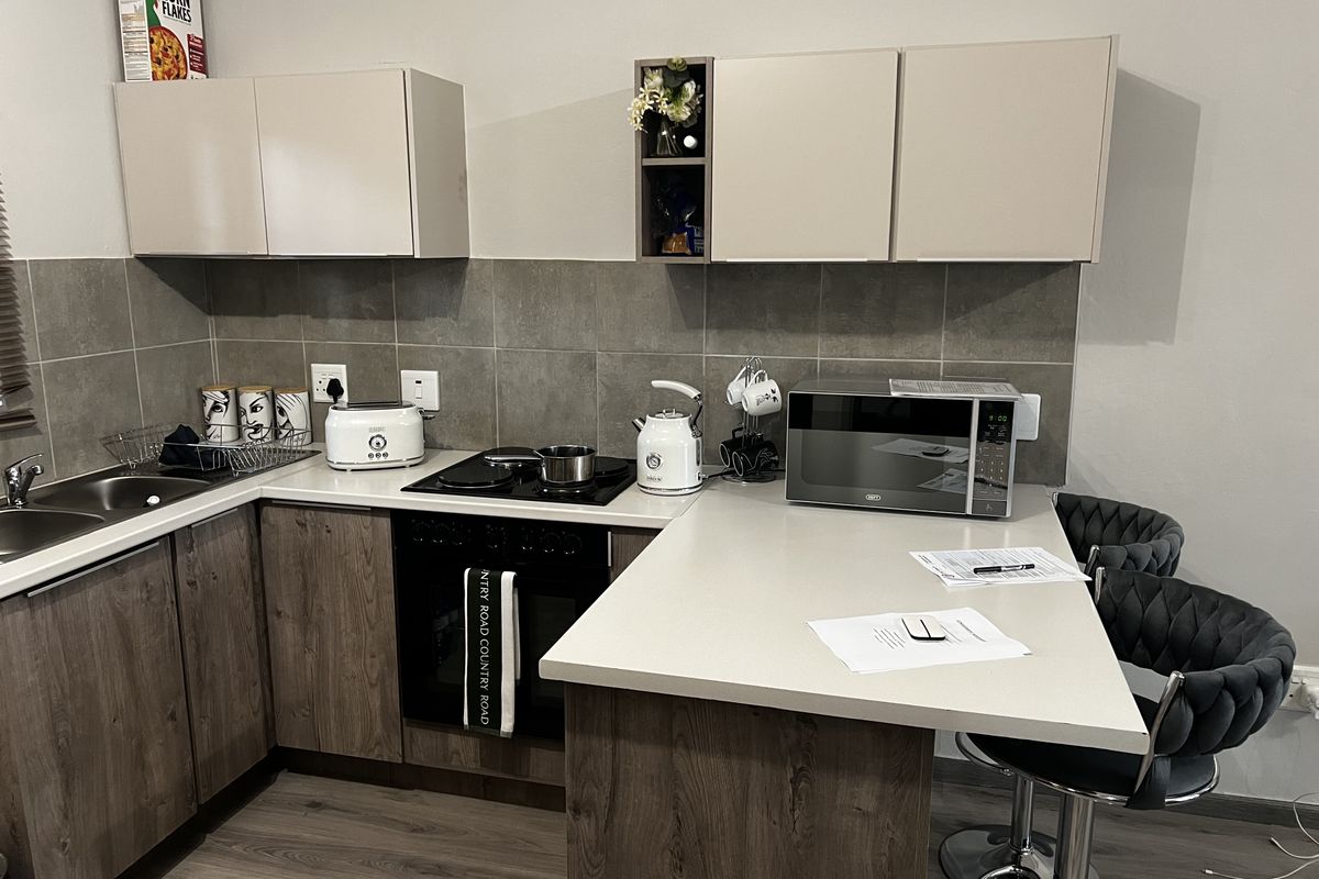 Modern kitchen featuring wood-grain cabinetry, stone-look countertops, a built-in oven with hob, and a tiled backsplash with an integrated breakfast bar.