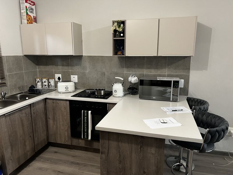 Modern kitchen featuring wood-grain cabinetry, stone-look countertops, a built-in oven with hob, and a tiled backsplash with an integrated breakfast bar.