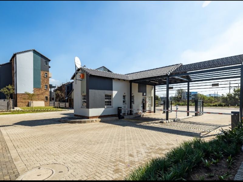 A secure gated entrance to the apartment complex featuring a guardhouse, paved driveway, and automated boom gate access control system.