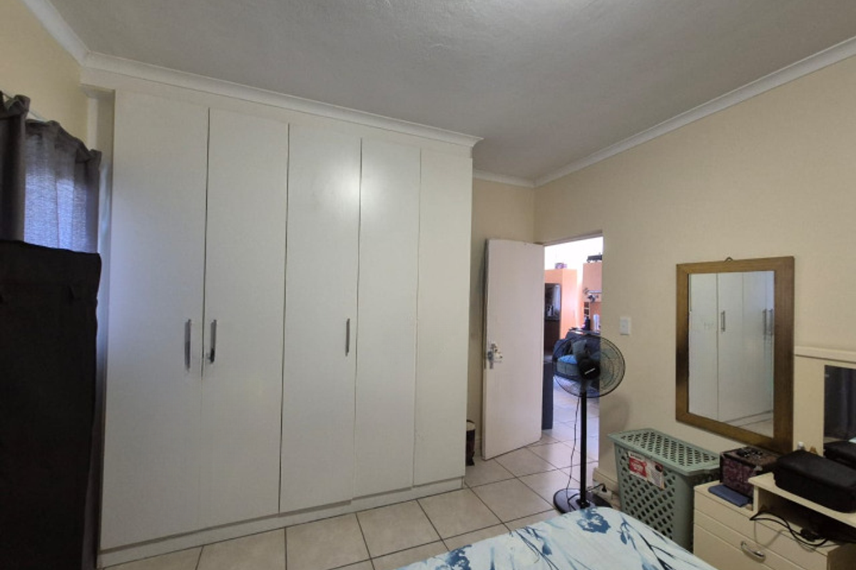 A bedroom featuring built-in floor-to-ceiling wardrobes, tiled flooring, and a doorway leading to an adjacent living space.