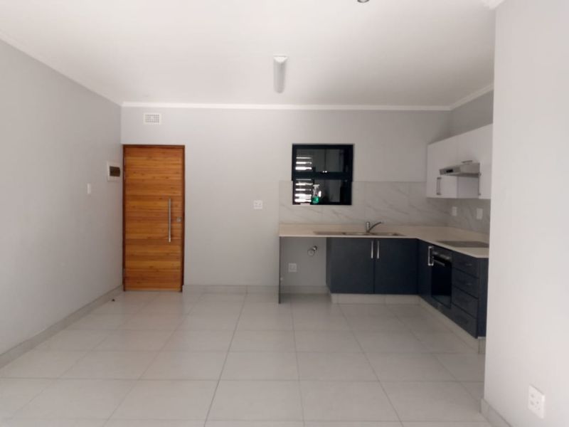 An open-plan kitchen featuring modern two-tone cabinetry, a built-in oven, extractor fan, and tiled flooring, adjacent to a wooden entrance door.