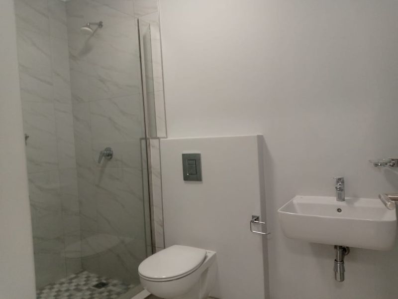 Modern bathroom featuring a wall-mounted toilet, a floating vanity sink, and a glass-enclosed shower with marble-look wall tiles.