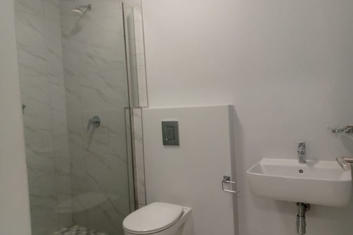 Modern bathroom featuring a wall-mounted toilet, a floating vanity sink, and a glass-enclosed shower with marble-look wall tiles.