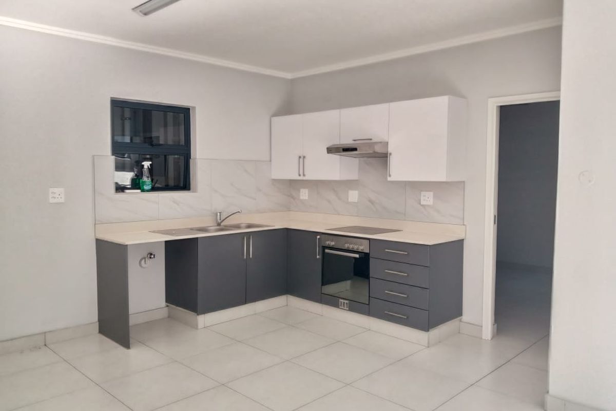 Modern kitchen featuring two-tone cabinetry, stone-look countertops, built-in oven, hob, and extractor fan with tiled flooring.