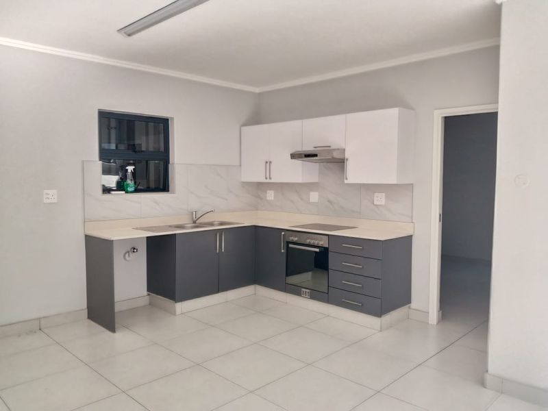 Modern kitchen featuring two-tone cabinetry, stone-look countertops, built-in oven, hob, and extractor fan with tiled flooring.