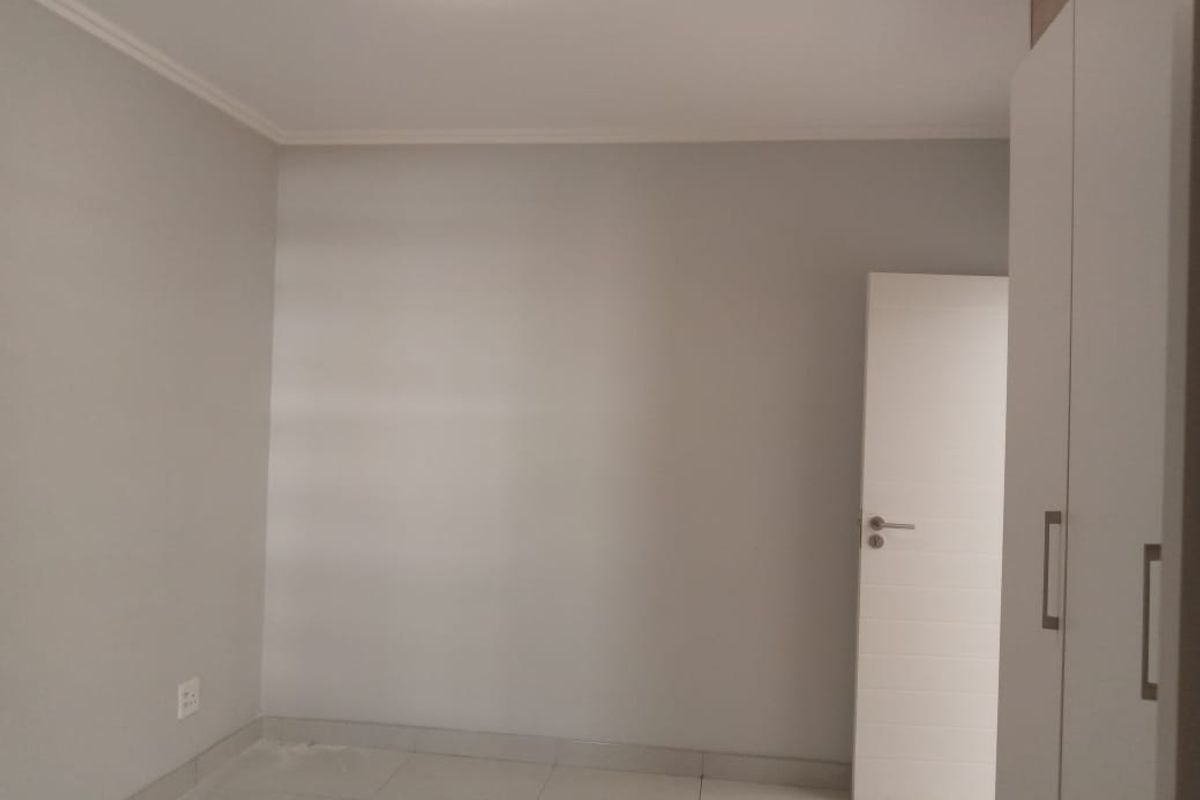 A clean, neutral bedroom featuring tiled flooring, built-in cabinetry, and a modern interior door.