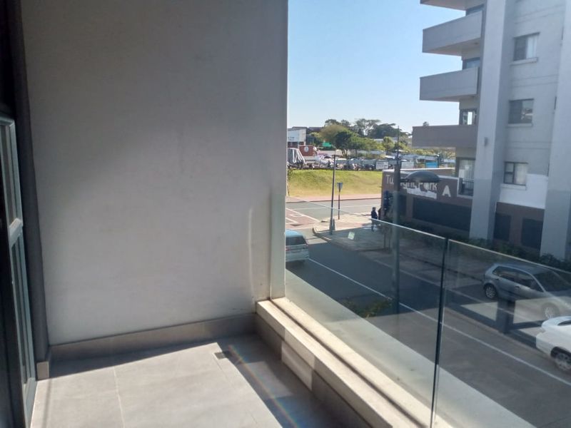 A modern apartment balcony featuring a glass balustrade and tiled flooring, offering an elevated view of the surrounding street and neighborhood.