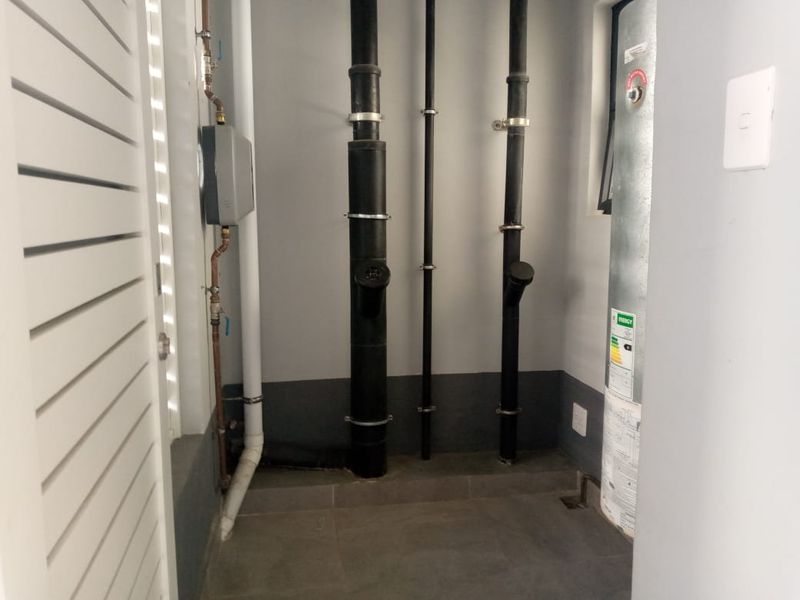 A utility space featuring exposed plumbing pipes, a water heater, and tiled flooring, providing functional access to essential building services.