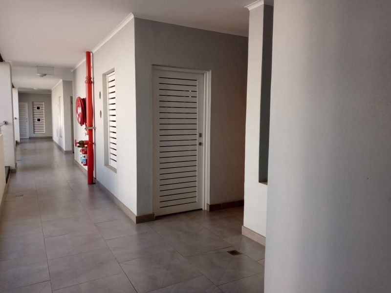 A clean, well-maintained apartment building hallway featuring tiled flooring, white louvered doors, and integrated fire safety equipment.