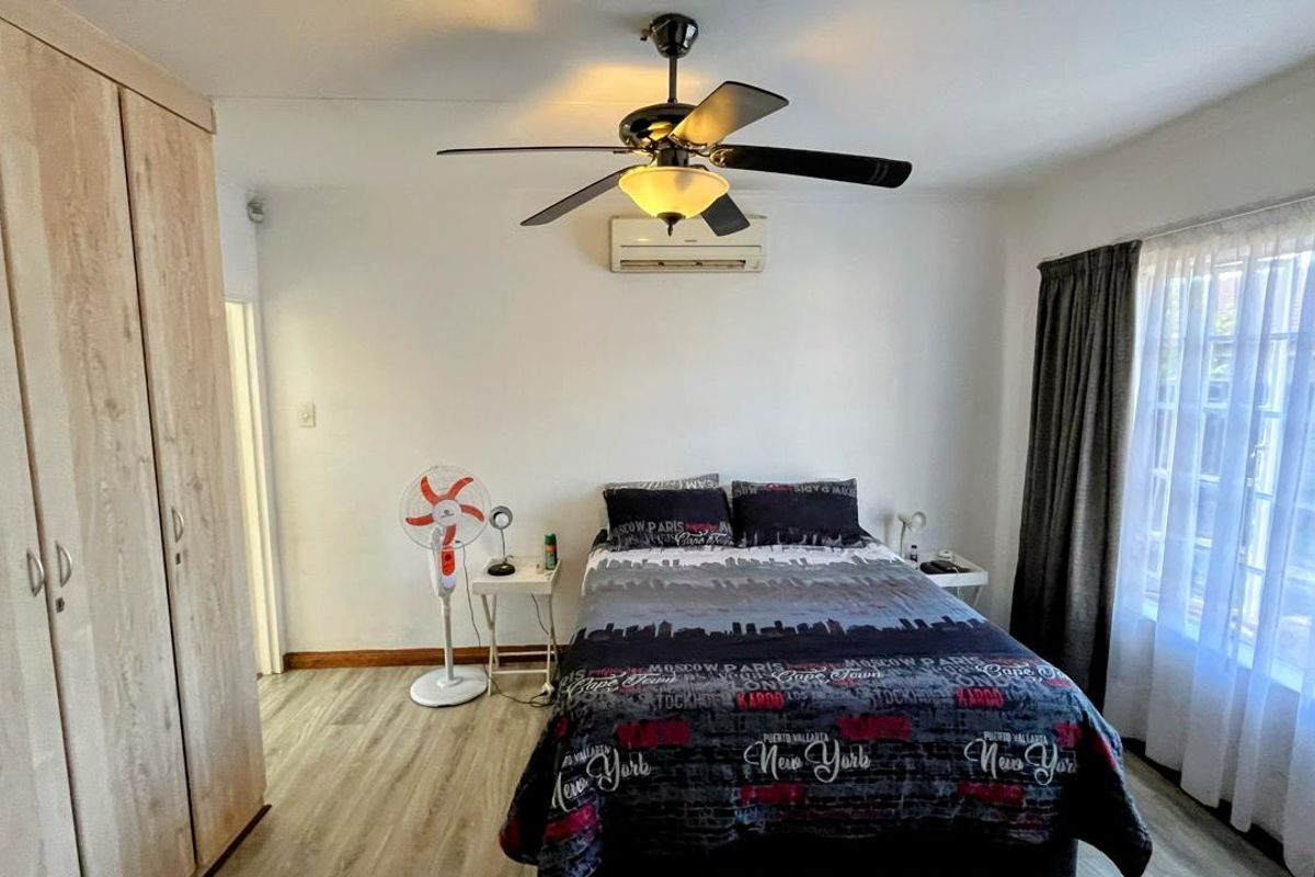 A well-lit bedroom featuring built-in wooden wardrobes, a ceiling fan, and a wall-mounted air conditioning unit, finished with light-toned wood-look flooring.