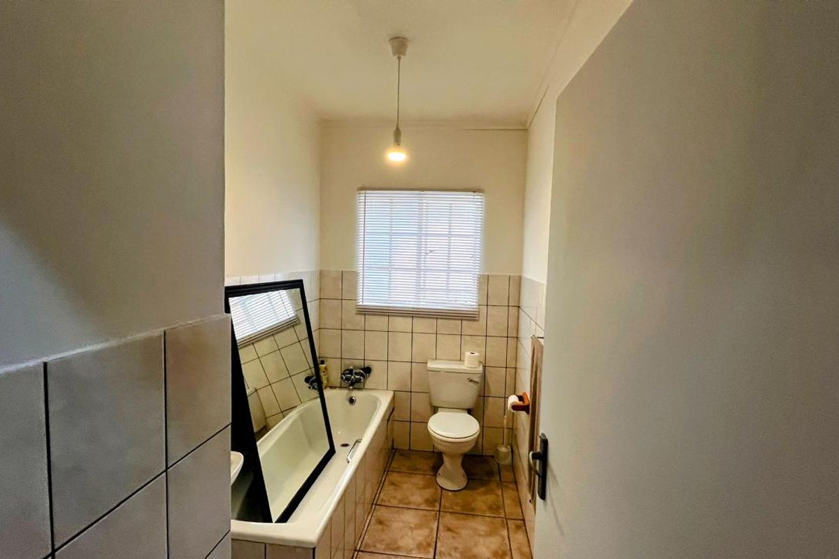 A functional bathroom featuring a bathtub, toilet, and tiled finishes, offering a practical layout with natural light from the window.