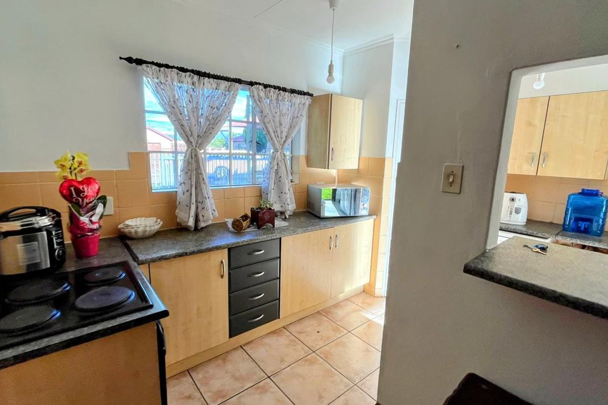 Functional kitchen featuring light wood cabinetry, laminate countertops, tiled backsplash, and a built-in electric hob, with a convenient pass-through window to the adjacent area.