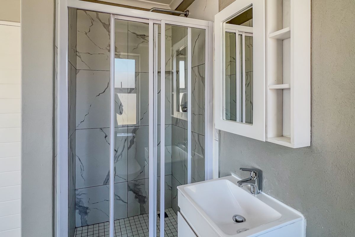 A modern bathroom featuring a glass-enclosed shower with marble-look wall tiles, a white vanity basin, and a built-in mirrored medicine cabinet.