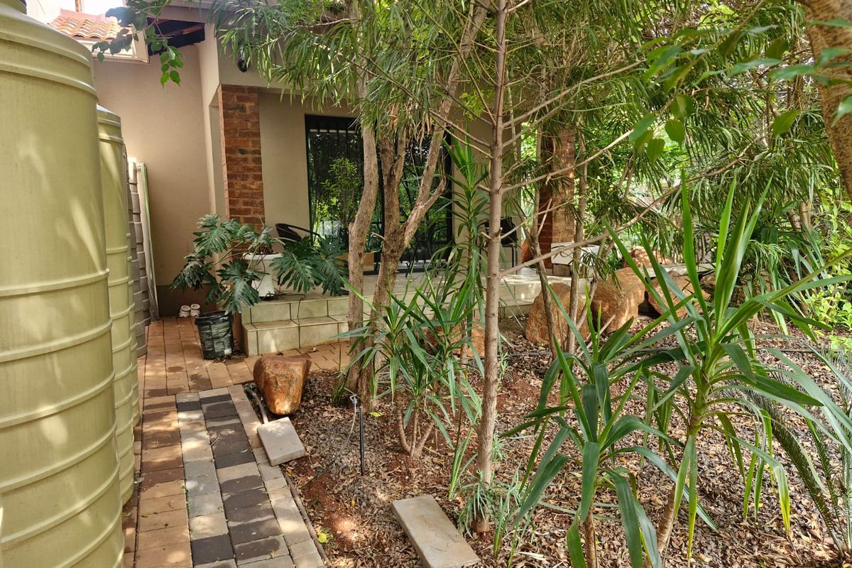 A view of the rear patio area featuring brick pillars, paved walkways, and large water storage tanks set within a landscaped garden.
