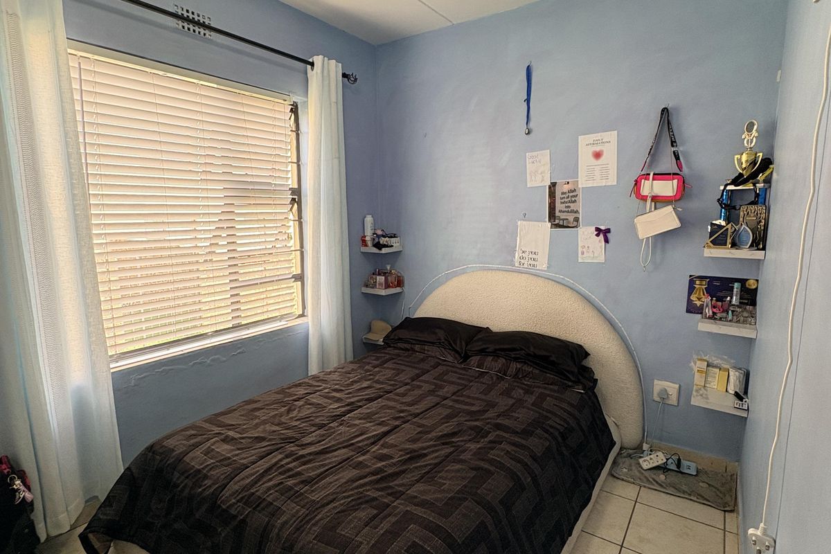 A compact bedroom featuring tiled flooring, a window with fitted blinds, and a wall-mounted air conditioning unit.