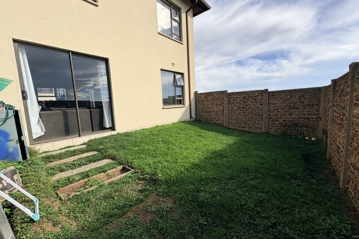 A private rear garden area featuring a grass lawn, concrete stepping stones, and a high boundary wall, accessible via sliding glass doors.