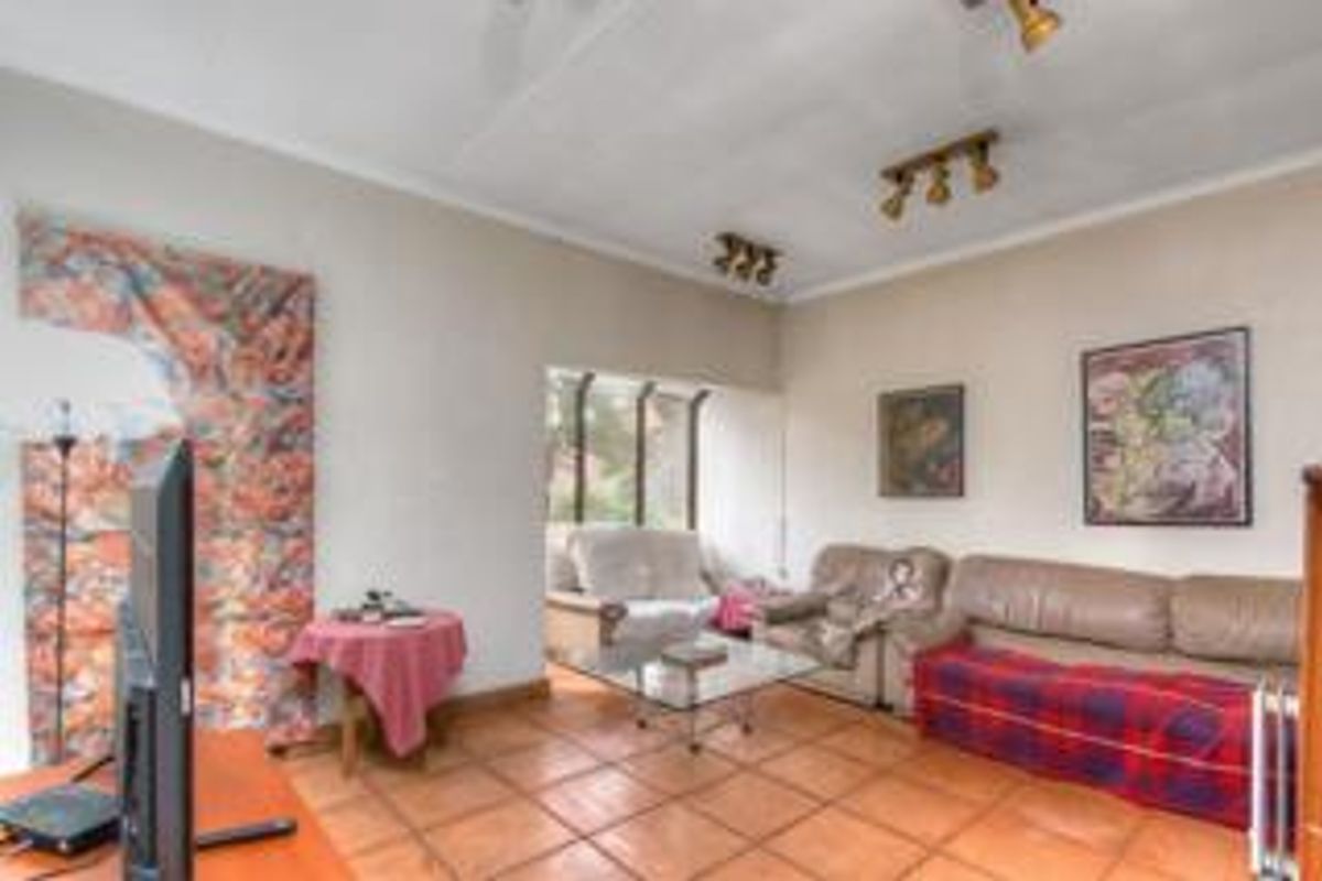 A living room featuring terracotta floor tiles, neutral walls, and multiple ceiling-mounted spotlights, providing a functional and well-lit living space.