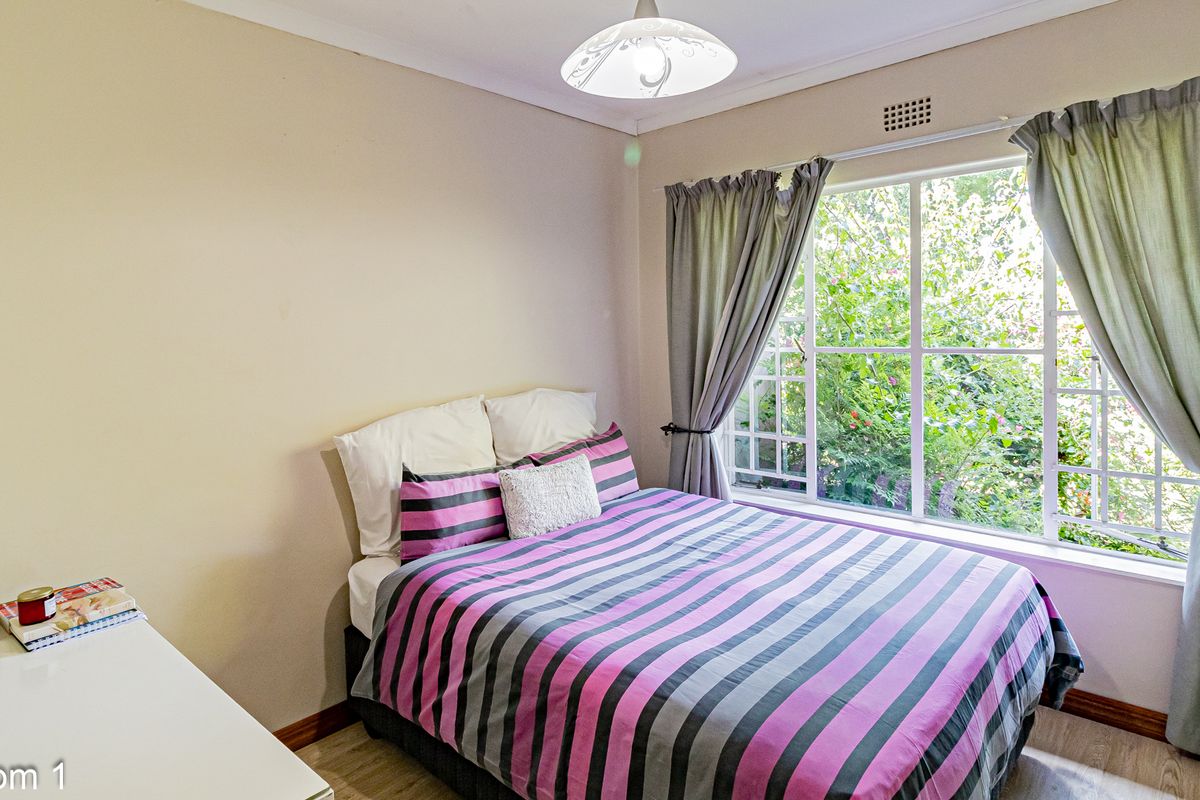 A bedroom featuring a large window with garden views, neutral wall finishes, and light-toned flooring.