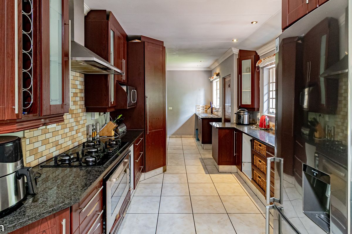 A functional kitchen featuring dark wood cabinetry, granite countertops, a built-in gas hob, extractor fan, and tiled flooring with a connected scullery area.