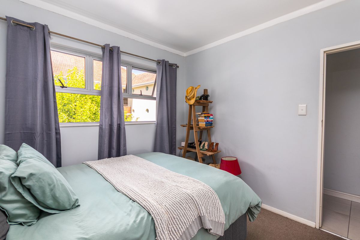A well-lit bedroom featuring neutral wall finishes, carpeted flooring, and large windows that provide natural light and a view of the surrounding area.